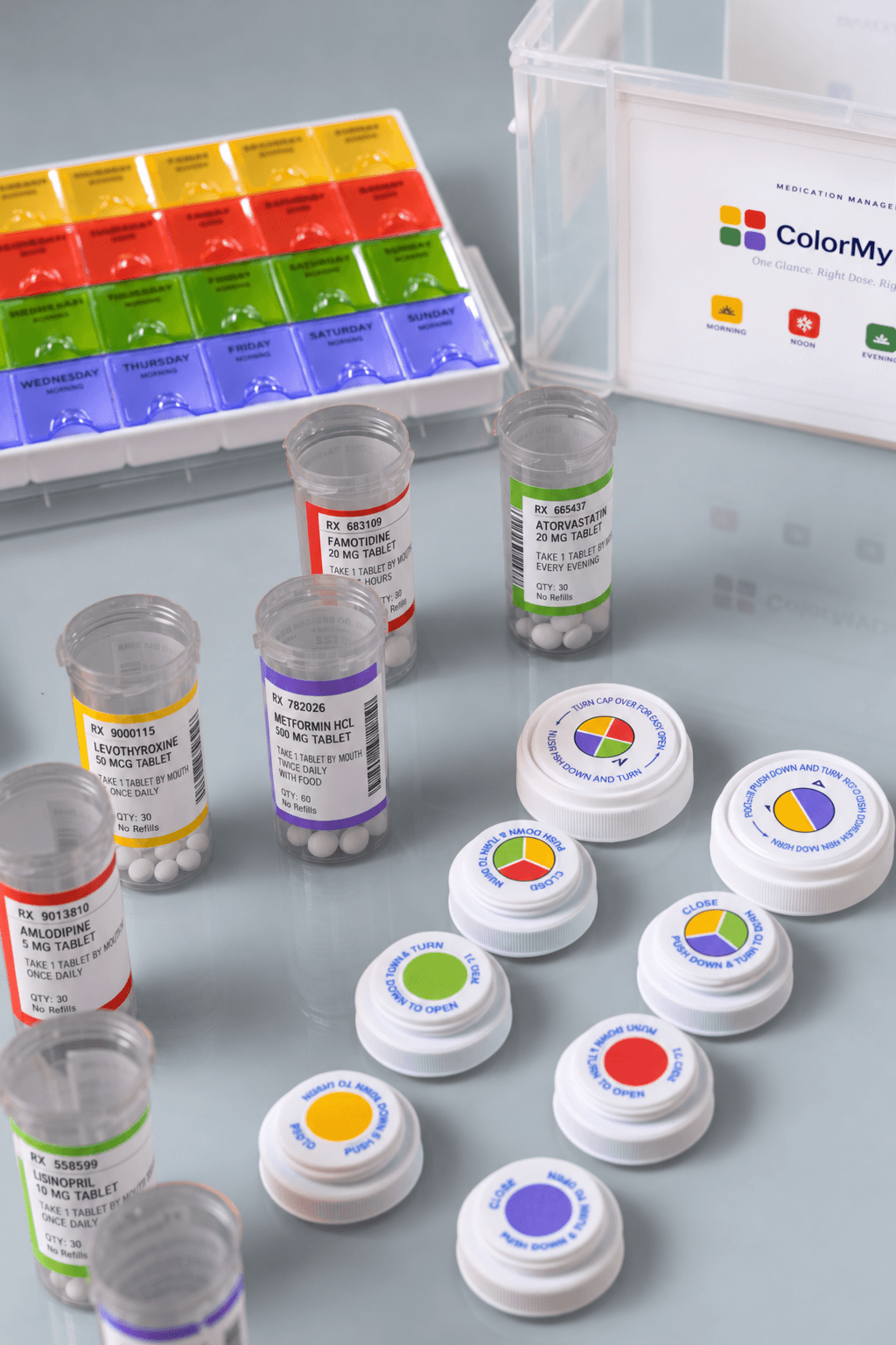 Prescription bottles on a pharmacy counter, each label printed with a colored dose band — yellow Morning, red Noon, green Evening, purple Bedtime — beside matching color-coded caps, a seven-day organizer, and the ColorMyDose kit case.